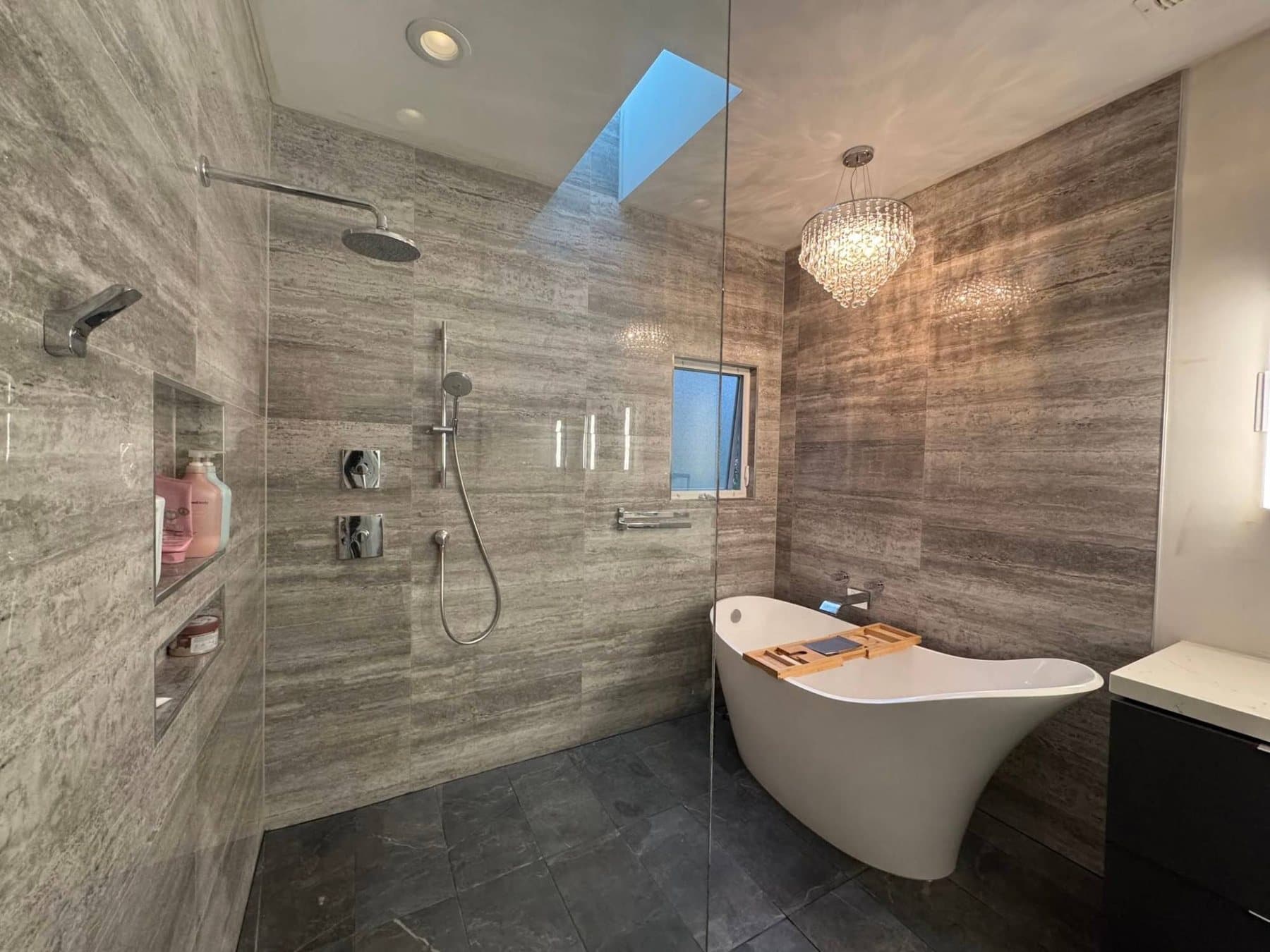 Wet-room bath with travertine-look tile, freestanding tub, and crystal chandelier